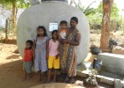 A family stands in front of their rainwater harvesting tank.