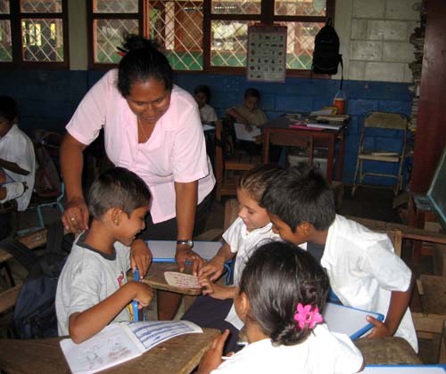 A teacher gets involved in the work of a group. She uses materials created by students and hung on the walls of the classroom.  