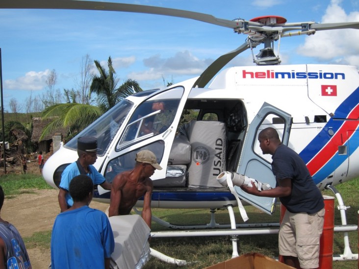 Men load plastic sheeting onto a helicopter