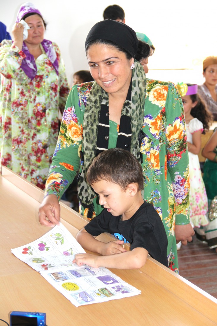 A boy reads a book provided by USAID with his teacher.