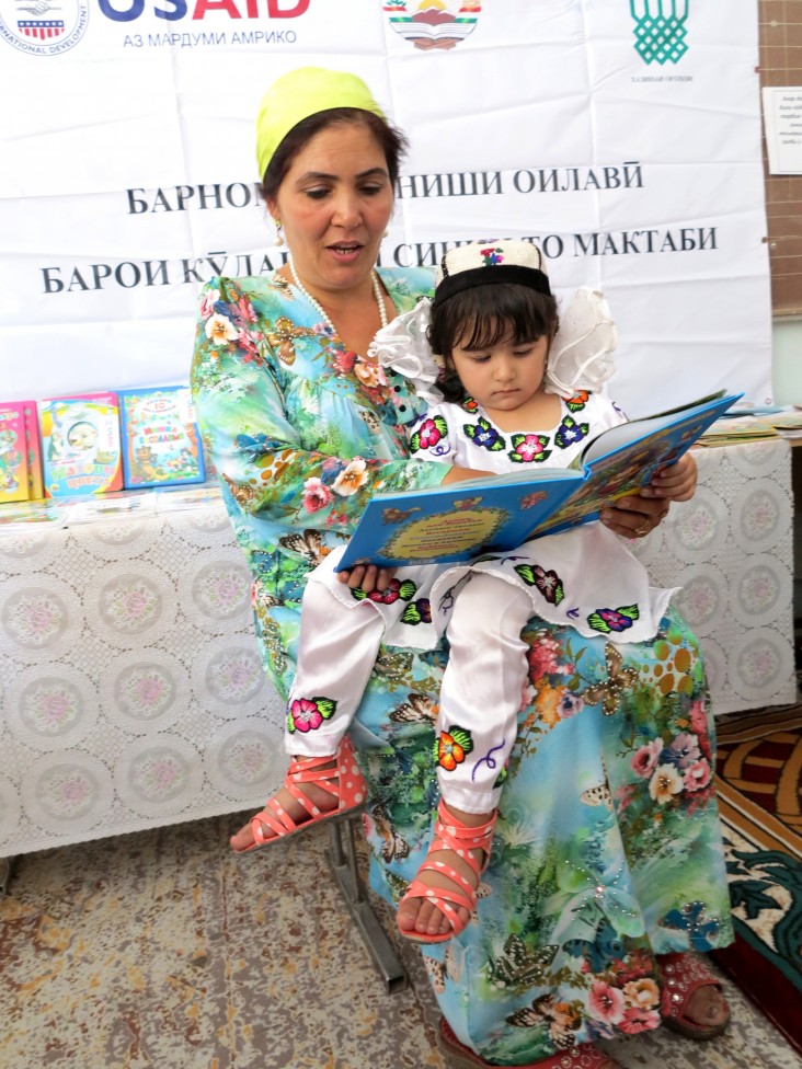 A teacher and student read together at a USAID event in Sarband, Tajikistan.