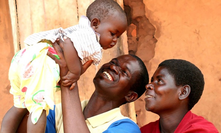 Photo of a father holding up his baby with the mother looking on.