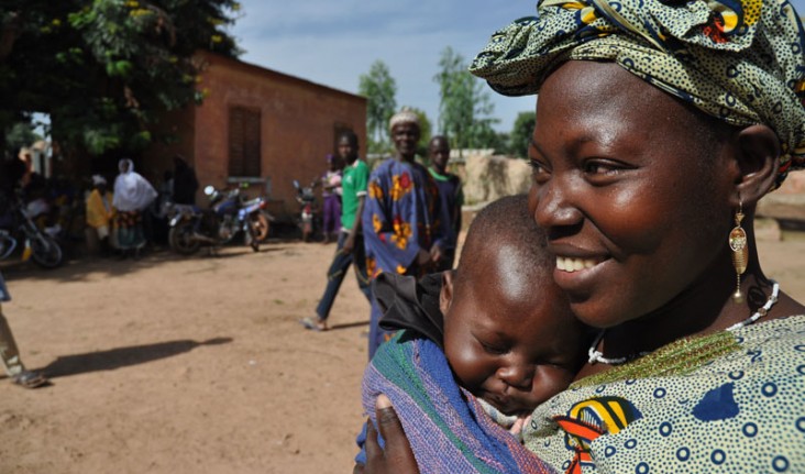 A woman holds her child, standing outside.