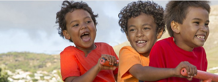 Three boys smile as they ride on a bike.