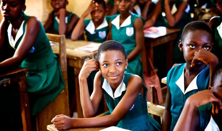 Adolescent girls in school uniforms sitting at their desks.