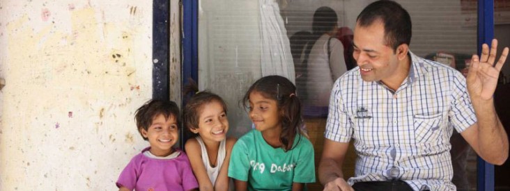 A man smiles down at three children sitting on a bench.