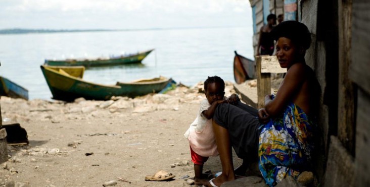 A mother and her child sit on the steps of their house by the water in Uganda