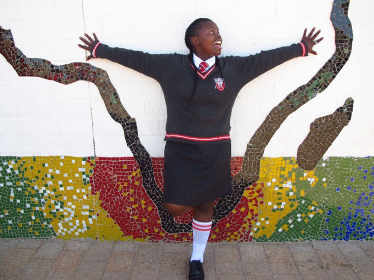 A young girl stands with arms up next to a colorful mural.