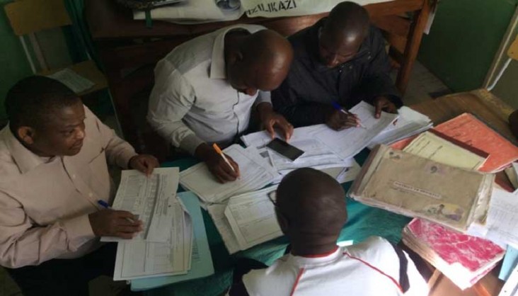 Four men sit around a table and look at papers.