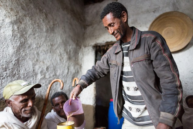 Berhe Desta serves a customer at his tella bet (an informal bar that sells local alcohol). Berhe and his wife Zenebu Shomoy work together in oxen fattening. They used some of the profit from their business to construct a new house for their family. Then they decided to generate additional income by using the front room of that house as a tella bet.