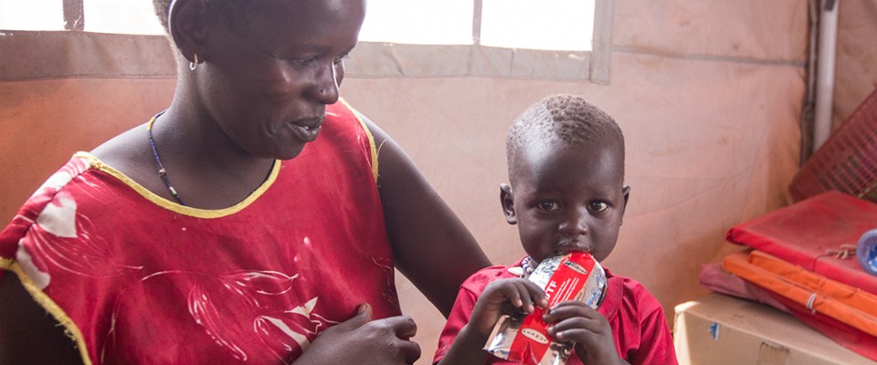 A mother is giving her malnourished baby ready-to-use therapeutic food from a packet.