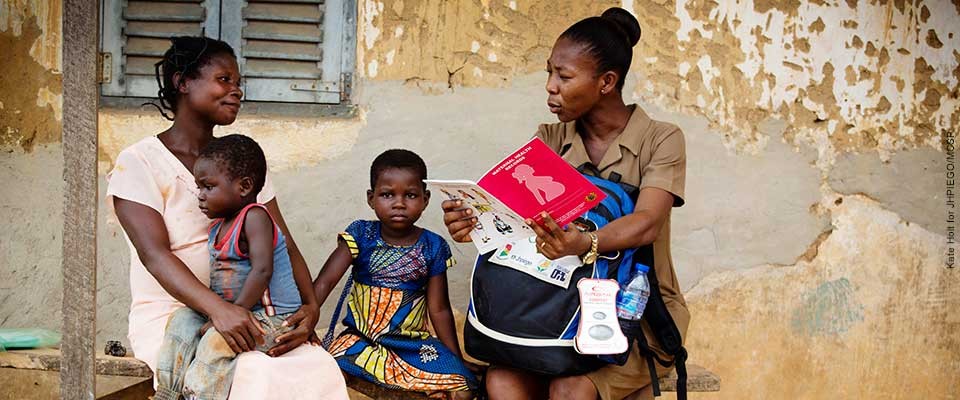 Two women sit with their babies in front of a building