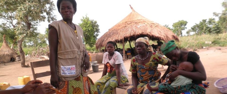 A community health worker speaks with three women and their babies outdoors.