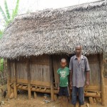 Rasolo and his son stand in front of their old home.