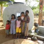 A family stands in front of their rainwater harvesting tank.