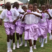 Two lines of Kenyan children wearing purple shorts march across a field